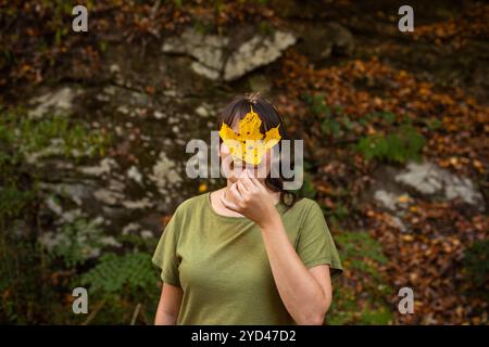 Frau in grünem Hemd, die gelbes Ahornblatt vor dem Gesicht hält Stockfoto