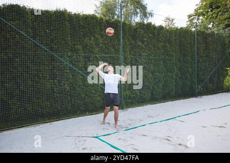 Volleyballspieler, der auf einem Sandplatz unter strahlend blauem Himmel Volleyball serviert. Eine dynamische Outdoor-Szene, perfekt für Sommersportarten und Beachvolleybale Stockfoto