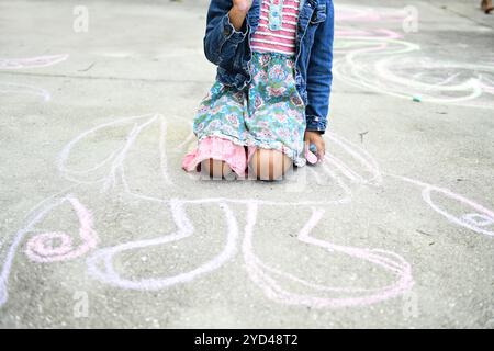 Kind kniet auf dem Gehweg, hält Kreide, große Kreidezeichnung b Stockfoto