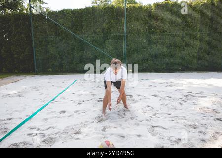 Volleyballspieler, der den Ball von einem Sandplatz abholt und sich auf das nächste Spiel in einem ungezwungenen Beachvolleyballspiel vorbereitet. In ruhiger Umgebung Stockfoto