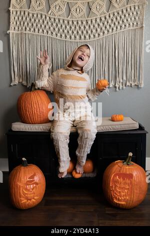 Kind im Mumienkostüm posiert mit Kürbissen in der Halloween-Szene drinnen Stockfoto