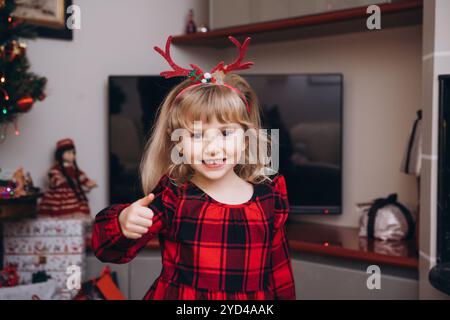 Ein schelmiges dreijähriges Mädchen in einem Weihnachtsoutfit mit Geweih Stockfoto