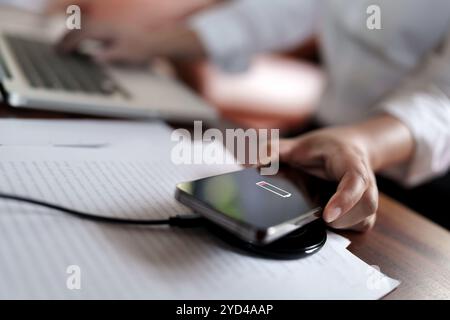 Frau lädt Mobiltelefon mit schnurlosem Schnellladegerät auf dem Desktop auf. Stockfoto