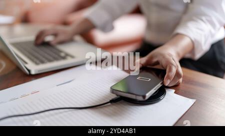 Frau lädt Mobiltelefon mit schnurlosem Schnellladegerät auf dem Desktop auf. Stockfoto