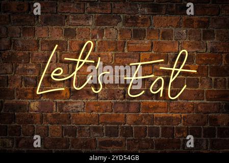 Ein leuchtendes gelbes Neonschild mit der Aufschrift Let's Eat in A Restaurant or Cafe Stockfoto