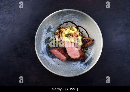 Traditionelles gebratenes Wildhasenfilet mit Pflaumen, Kapern und Kartoffelsalat in Rotwein-Jus serviert als Blick von oben auf dem nordischen Design-Teller mit Kopierraum Stockfoto