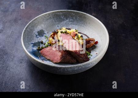 Traditionelles gebratenes Wildhasenfilet mit Pflaumen, Kapern und Kartoffelsalat in Rotwein-Jus, serviert als Nahaufnahme auf nordischem Design-Teller Stockfoto