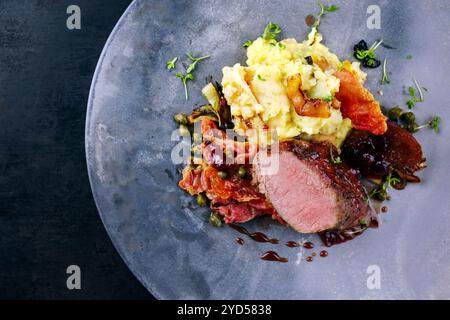 Traditionelles gebratenes Wildhasenfilet mit Pflaumen, Kapern und Kartoffelsalat in Rotwein-Jus serviert als Draufsicht auf nordischem Design-Teller mit Kopierraum r Stockfoto