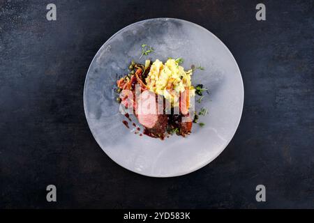 Traditionelles gebratenes Wildhasenfilet mit Pflaumen, Kapern und Kartoffelsalat in Rotwein-Jus serviert als Blick von oben auf dem nordischen Design-Teller mit Kopierraum Stockfoto