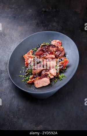 Traditionelles gebratenes Wildhasenfilet mit Pflaumen, Preiselbeeren und Speck in Rotwein-Jus, das als Nahaufnahme auf nordischem Design serviert wird Stockfoto