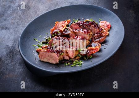 Traditionelles gebratenes Wildhasenfilet mit Pflaumen, Preiselbeeren und Speck in Rotwein-Jus, das als Nahaufnahme auf nordischem Design serviert wird Stockfoto