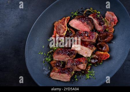 Traditionelles gebratenes Wildhasenfilet mit Pflaumen, Preiselbeeren und Speck in Rotwein-Jus serviert als Blick von oben auf dem nordischen Design-Teller mit Kopierraum Stockfoto