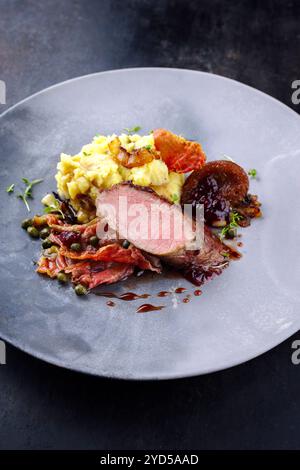 Traditionelles gebratenes Wildhasenfilet mit Pflaumen, Kapern und Kartoffelsalat in Rotwein-Jus, serviert als Nahaufnahme auf nordischem Design-Teller Stockfoto