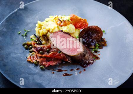 Traditionelles gebratenes Wildhasenfilet mit Pflaumen, Kapern und Kartoffelsalat in Rotwein-Jus, serviert als Nahaufnahme auf nordischem Design-Teller Stockfoto