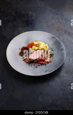 Traditionelles gebratenes Wildhasenfilet mit Pflaumen, Kapern und Kartoffelsalat in Rotwein-Jus, serviert als Nahaufnahme auf nordischem Design-Teller mit Kopierraum Stockfoto