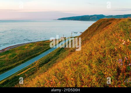 Malerische Aussicht von der Spitze des Hügels auf der Küstenstraße entlang des Meeres bei Sonnenuntergang. Nevelsk, Sachalin, Russland Stockfoto