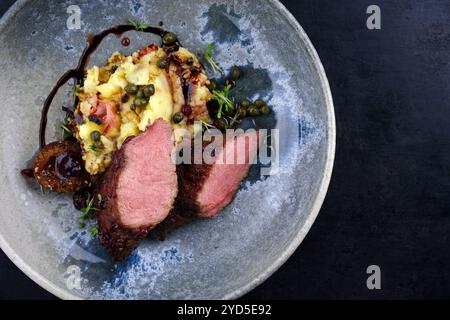 Traditionelles gebratenes Wildhasenfilet mit Pflaumen, Kapern und Kartoffelsalat in Rotwein-Jus serviert als Draufsicht auf nordischem Design-Teller mit Kopierraum r Stockfoto