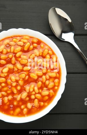 Weiße Bohnen in Tomatensauce in einer weißen Schüssel auf schwarzem Hintergrund. Draufsicht Stockfoto