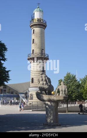 Rostock, Warnemünde, Deutschland 06-28-2024 Leuchtturm und Teekanne mit Skulptur Menschen in einem Boot Stockfoto