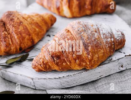 Schließen Sie frisch gebackene Croissants mit Zuckerpulver auf einem Holztisch Stockfoto