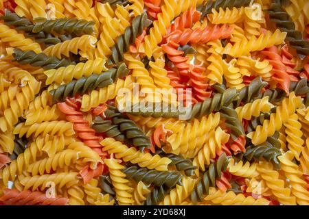 Ungekochte Fusilli Pasta in leuchtenden Farben: Eine faszinierende kulinarische Leinwand aus bunten Spiralen, die einen lebendigen und strukturierten Hintergrund für Gourmet-Kochen schafft. Farbige Trockene Pasta. Rohe Makkaroni Stockfoto