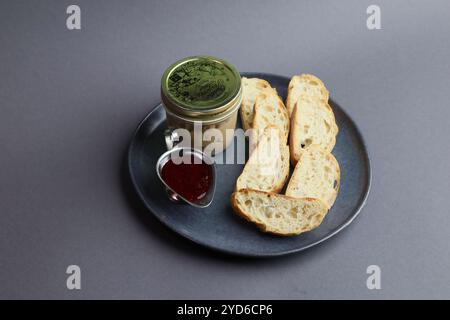 Zartes Hühnerleber-Mousse auf einer Keramikplatte neben weißen Baguette- und Beerenmarmelade. Stockfoto