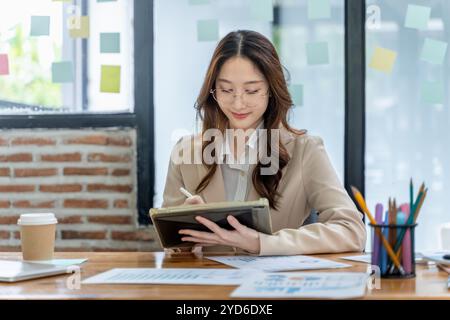 Glückliche junge Geschäftsfrau, die allein im Büro an ihrem Projekt arbeitet Stockfoto