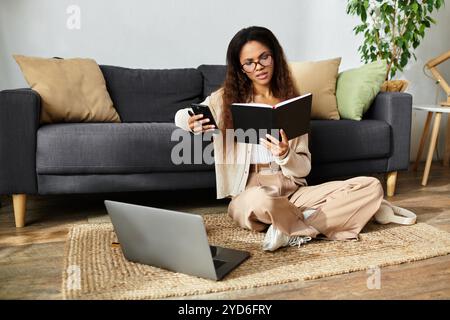 Eine Frau, die bequem auf dem Boden sitzt, liest ein Buch, checkt ihr Smartphone und genießt ihre Zeit. Stockfoto