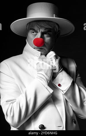 Nahaufnahme selektives Farbporträt des traurigen Clowns. Ein älterer Mann mit weißem Mantel und Hut. Stockfoto