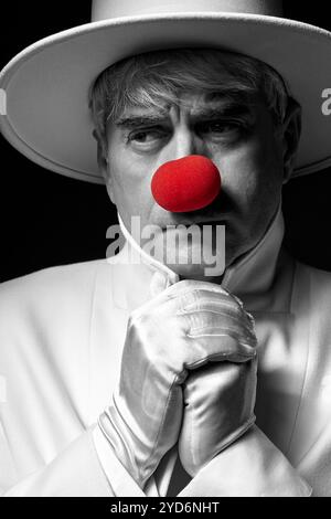 Nahaufnahme selektives Farbporträt des traurigen Clowns. Ein älterer Mann mit weißem Mantel und Hut. Stockfoto