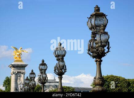 Wunderschöne Schmiedelampen und goldene Statuen der Alexander III Brücke unter blauem Himmel. Paris, Frankreich. Petit palais Museum Dach im Hintergrund. Stockfoto