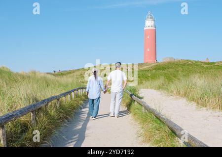 Ein Paar spaziert gemütlich entlang eines Küstenweges, mit einem wunderschönen Leuchtturm im Hintergrund, unter einem klaren Himmel auf Texel Islan Stockfoto