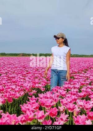 Eine Frau steht elegant in einem Feld aus leuchtend rosa Tulpen, umgeben von ihrer Schönheit und Gelassenheit Stockfoto