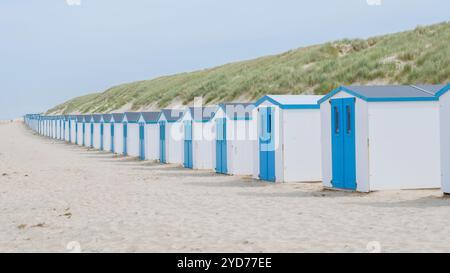 Eine bezaubernde Reihe von blau-weißen Strandhütten, die hoch an den Sandstränden stehen und eine malerische Szene vor dem klaren bl schaffen Stockfoto