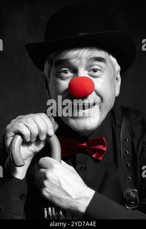 Selektives Farbporträt eines lachenden Clowns vor dunklem Hintergrund am Griff eines Regenschirms. Stockfoto