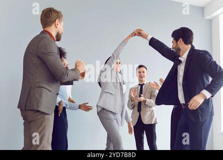 Eine Gruppe von glücklichen Geschäftsleuten, Männer und Frauen in Anzügen, die im Büro tanzt. Stockfoto