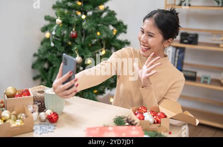 Glückliche junge Frau, die smartphoneÂ mobil sucht, verbringt Zeit vor dem Weihnachtsbaum zu Hause, um Neujahr und Chri zu feiern Stockfoto