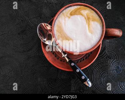 Eine köstliche Tasse Kaffee mit cremiger Crema serviert in einem rustikalen Glas. Tongeschirr auf schwarzem Hintergrund, Draufsicht. Cappuccino in braunem Becher auf Untertasse mit s Stockfoto