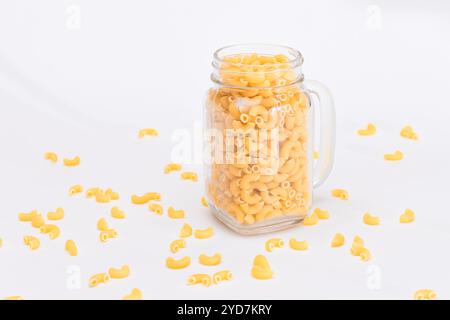 Ungekochte Chifferi Rigati Pasta in Glasglas auf weißem Hintergrund. Fett und ungesunde Lebensmittel. Verstreute Klassische Trockene Makkaroni. Italienische Kultur und Küche. Rohe Pasta Stockfoto