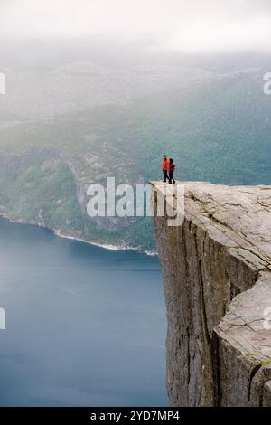 Preikestolen, Norwegen, zwei Menschen stehen am Rande einer Klippe mit Blick auf einen Fjord in Norwegen. Die Klippe ist bekannt als Preikestolen. Stockfoto