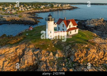 Nubble Lighthouse mit weißem Turm und rotem Dachhaus steht auf einer felsigen Klippe mit Blick auf das ruhige Meer. In der Nähe gibt es einen kleinen roten Schuppen und einen Di Stockfoto