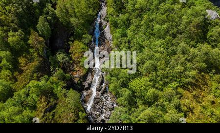 Ein Blick aus der Vogelperspektive auf einen kaskadierenden Wasserfall, der durch einen dichten Wald in Norwegen fließt Stockfoto