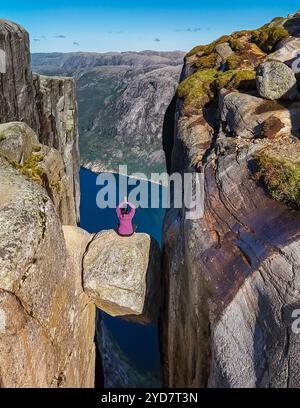 Eine Person sitzt am Rande von Kjeragbolten, Norwegen, einer berühmten Klippe in Norwegen, mit Blick auf die umliegende Landschaft und den fj Stockfoto