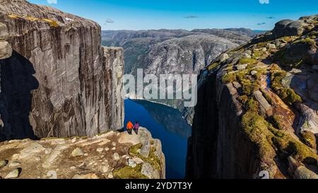 Zwei Wanderer stehen am Rande von Kjeragbolten, Norwegen, einer berühmten Klippe in Norwegen, mit einem atemberaubenden Blick auf den umliegenden Fjord. Ein paar Männer und W Stockfoto