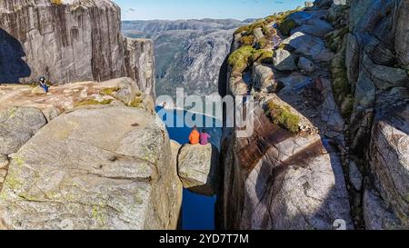 Zwei Wanderer sitzen am Rande des Kjeragbolten Pulpit Rock in Norwegen und genießen den atemberaubenden Panoramablick auf die umliegenden Berge Stockfoto