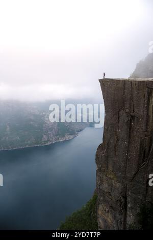 Ein einsames Individuum steht am Rande von Preikestolen, einer Klippe in Norwegen mit Blick auf einen Fjord. Stockfoto