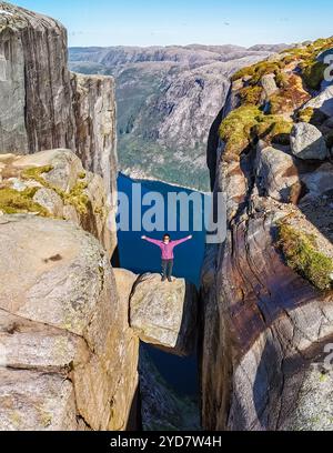 Eine Person steht auf einer schmalen Felsformation mit Blick auf den atemberaubenden Fjord Kjeragbolten, Norwegen Stockfoto