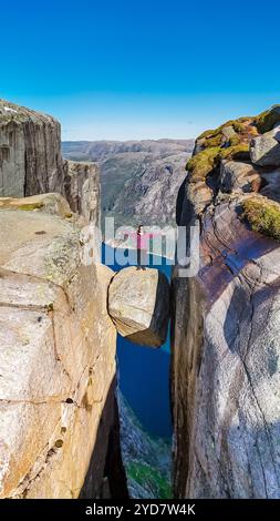 Eine Frau steht am Rande von Kjeragbolten, Norwegen, einer berühmten Klippe in Norwegen. Die Aussicht von oben ist atemberaubend, mit einem tiefen Stockfoto