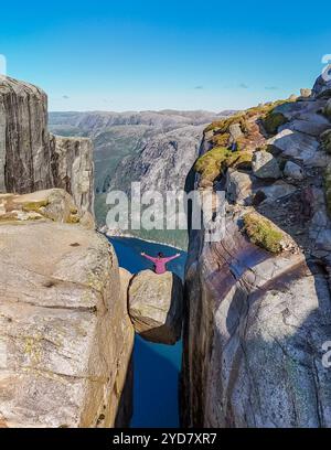 Ein einsamer Wanderer sitzt auf einem Felsen mit Blick auf eine dramatische Klippe in Kjeragbolten Norwegen Stockfoto