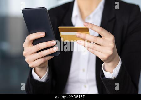 Geschäftsfrau hat Smartphone und Kreditkarte und führt Online-Zahlungen durch. Professionelle Kleidung bietet eine Büroumgebung. Veranschaulicht digitale Transaktionen, Sicherheit und Bequemlichkeit in modernen Geschäftsbereichen. Stockfoto